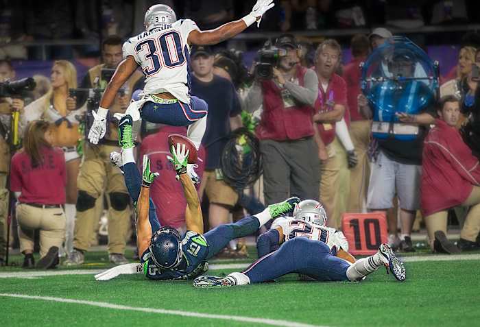 On his back, Jermaine Kearse reaches for a catch between two Patriots defenders during the fourth quarter of Super Bowl 49